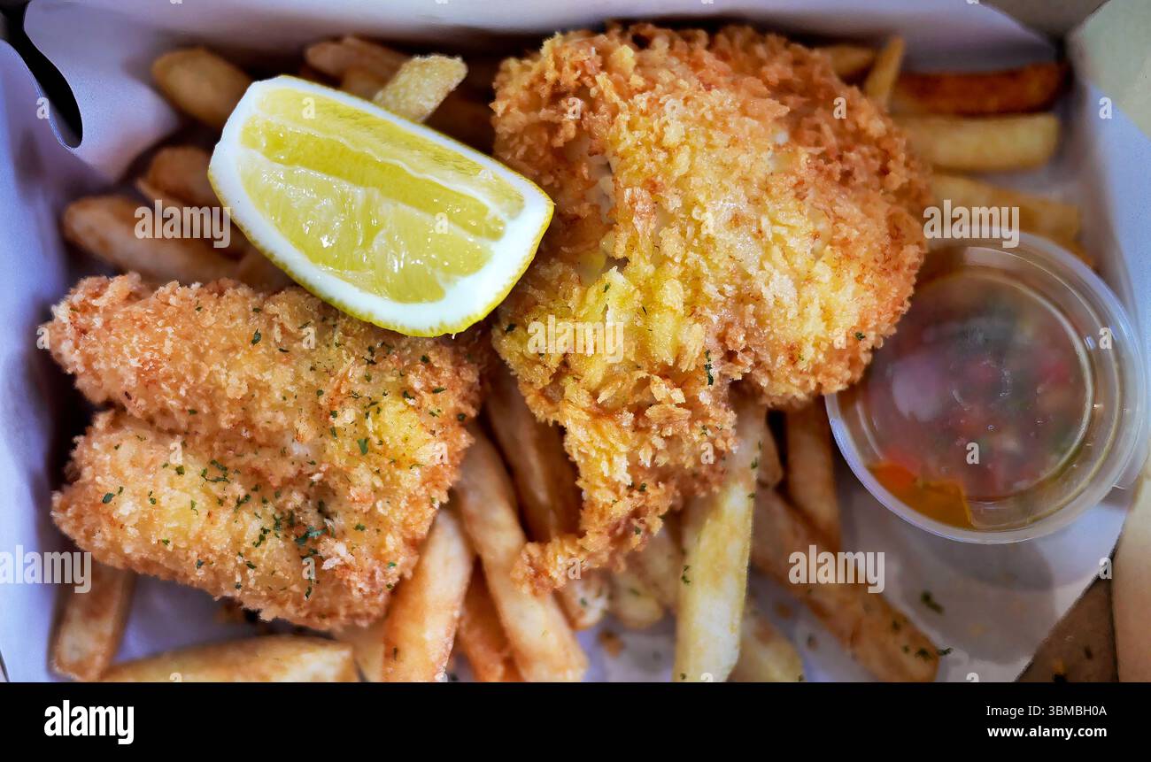 Classique traditionnel anglais ou britannique délice culinaire Fish and Chips, poisson frit doré avec quartiers de citron dans une boîte en papier à emporter comme déjeuner Banque D'Images