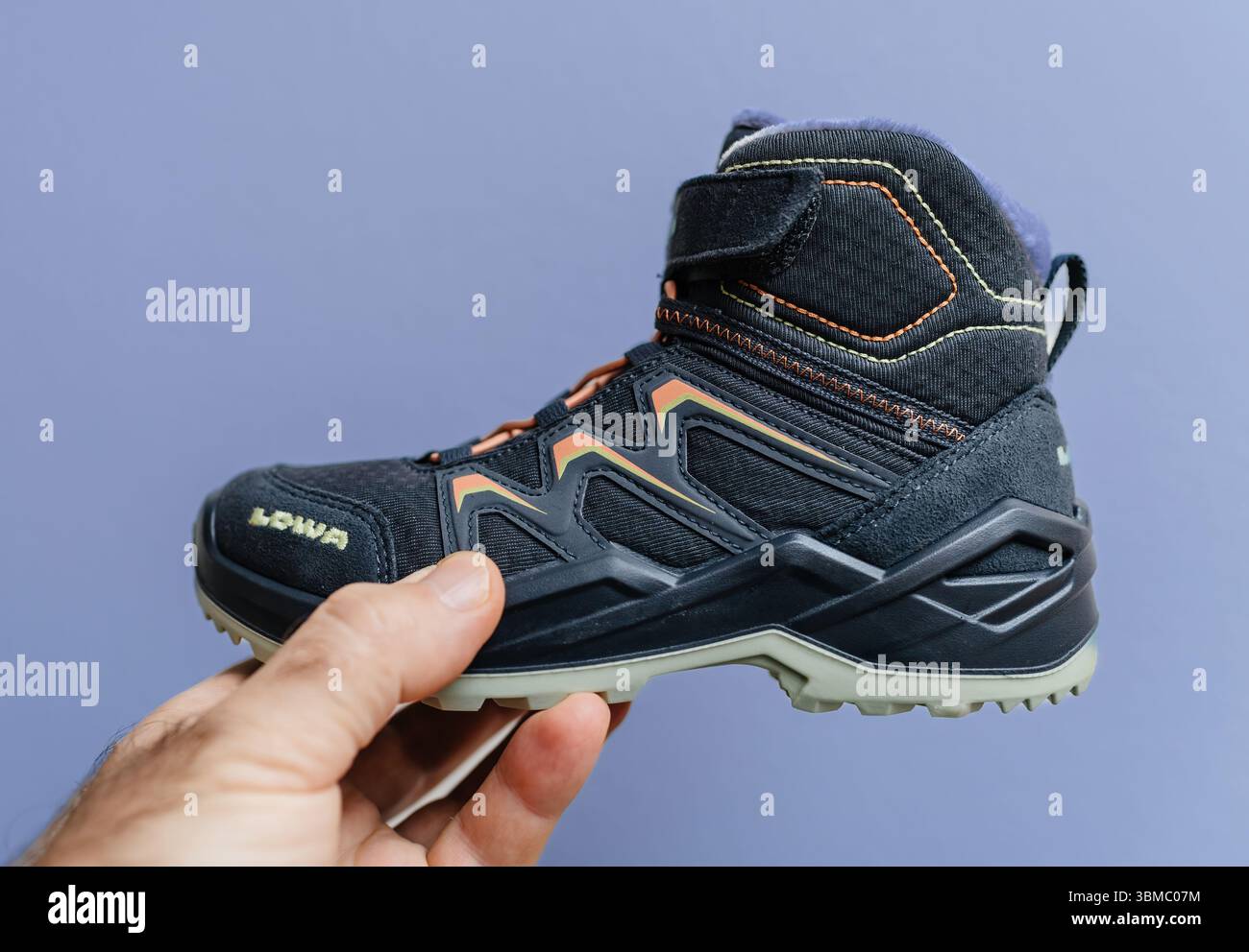 Paris, France - 24 nov. 2024 : une main tient une chaussure tout-terrain LOWA basse pour enfants en noir avec coutures orange et jaune, visible t Banque D'Images