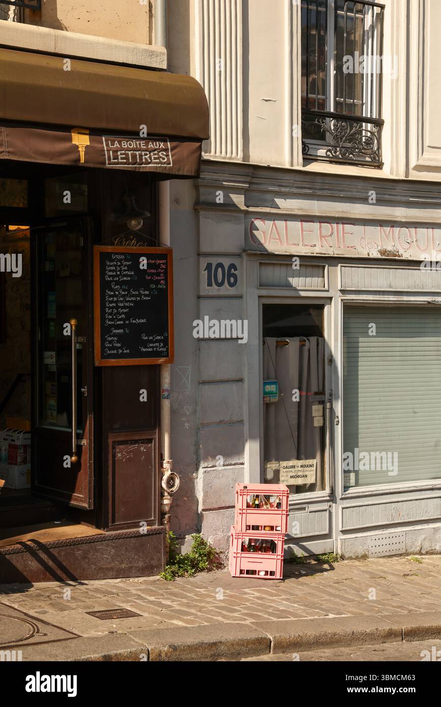 Une charmante scène de rue parisienne avec un café avec un menu en tableau noir, deux caisses roses remplies de bouteilles, et une façade de bâtiment vintage avec weat Banque D'Images