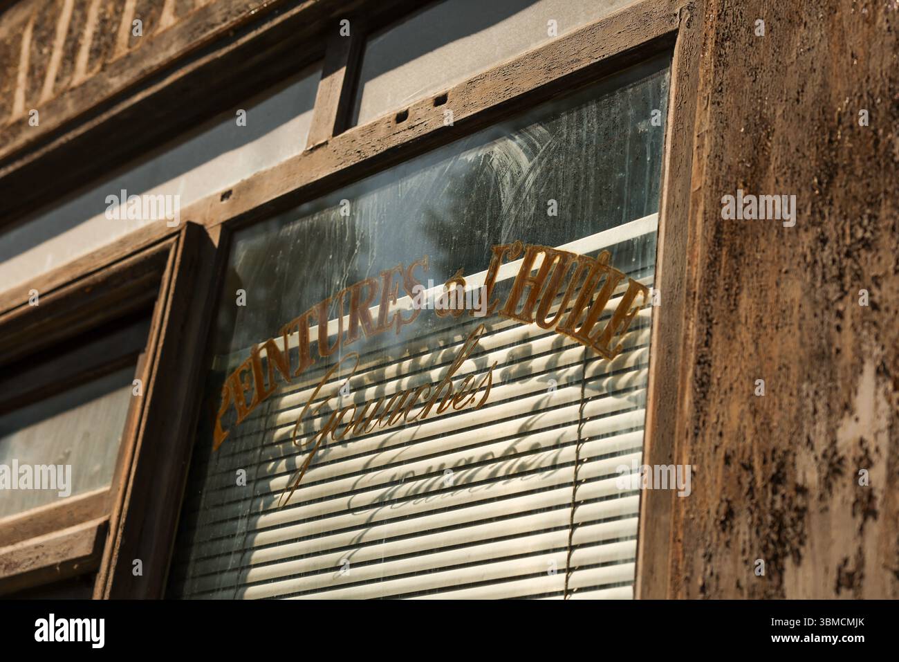 Gros plan d'un cadre de fenêtre en bois altéré d'un vieux magasin. Un panneau doré délavé indiquant « peintures a l'huile » est visible sur le verre poussiéreux, derrière Banque D'Images
