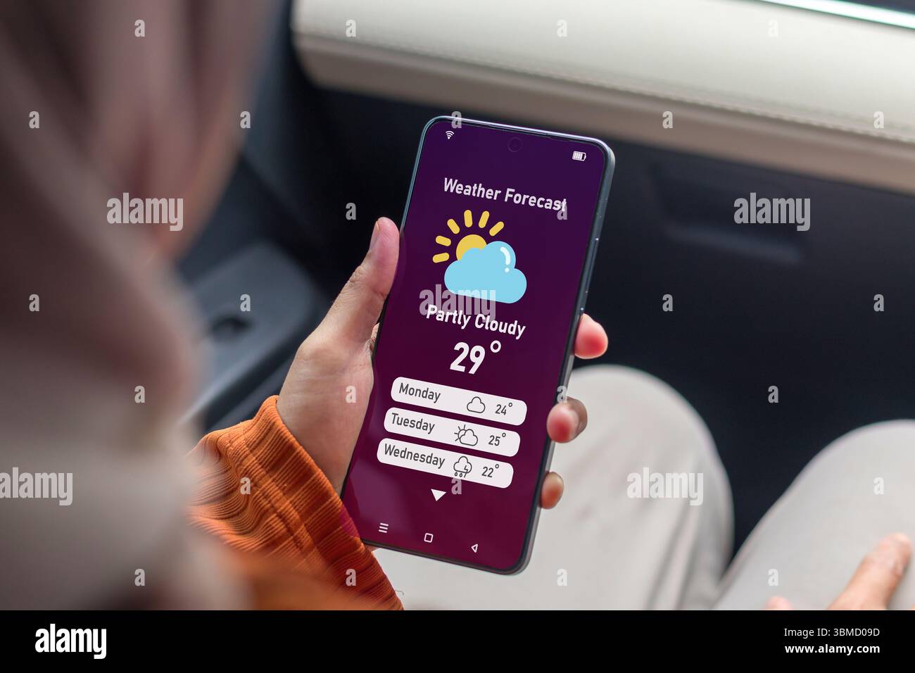 Une femme musulmane dans une voiture vérifiant les prévisions météorologiques à l'aide d'une application sur son smartphone Banque D'Images