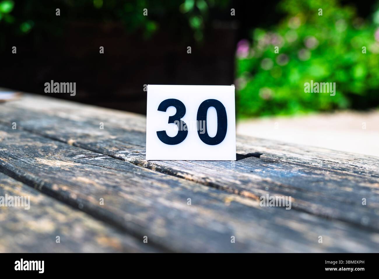 Un panneau blanc affichant le numéro 30 sur une surface en bois altérée à l'extérieur. Un numéro de table pour un événement ou marquer un jalon significatif comme un 30e. Banque D'Images