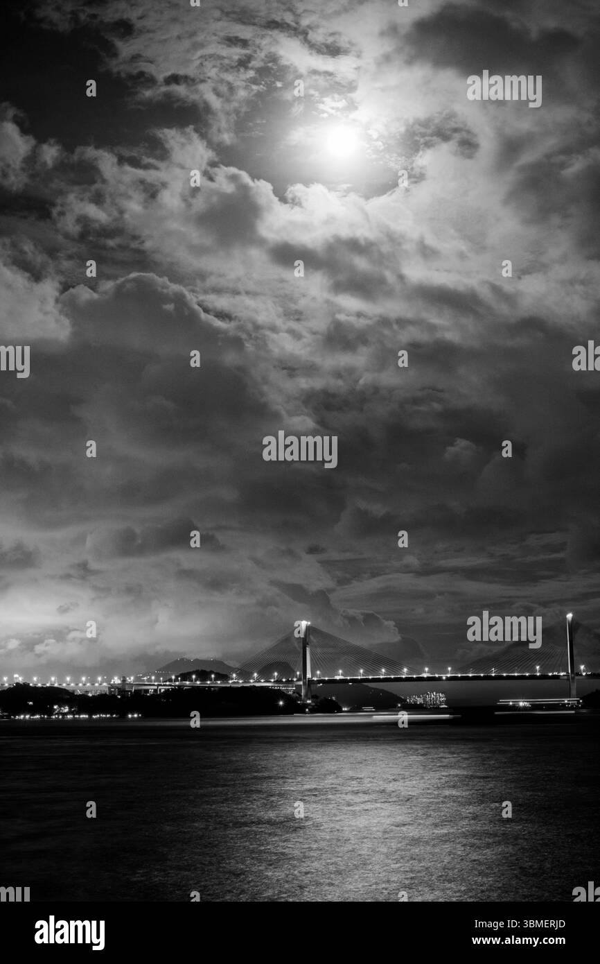Image en noir et blanc du pont de Tsing ma à Hong Kong, illuminé par le clair de lune, avec un ciel spectaculaire rempli de nuages Banque D'Images