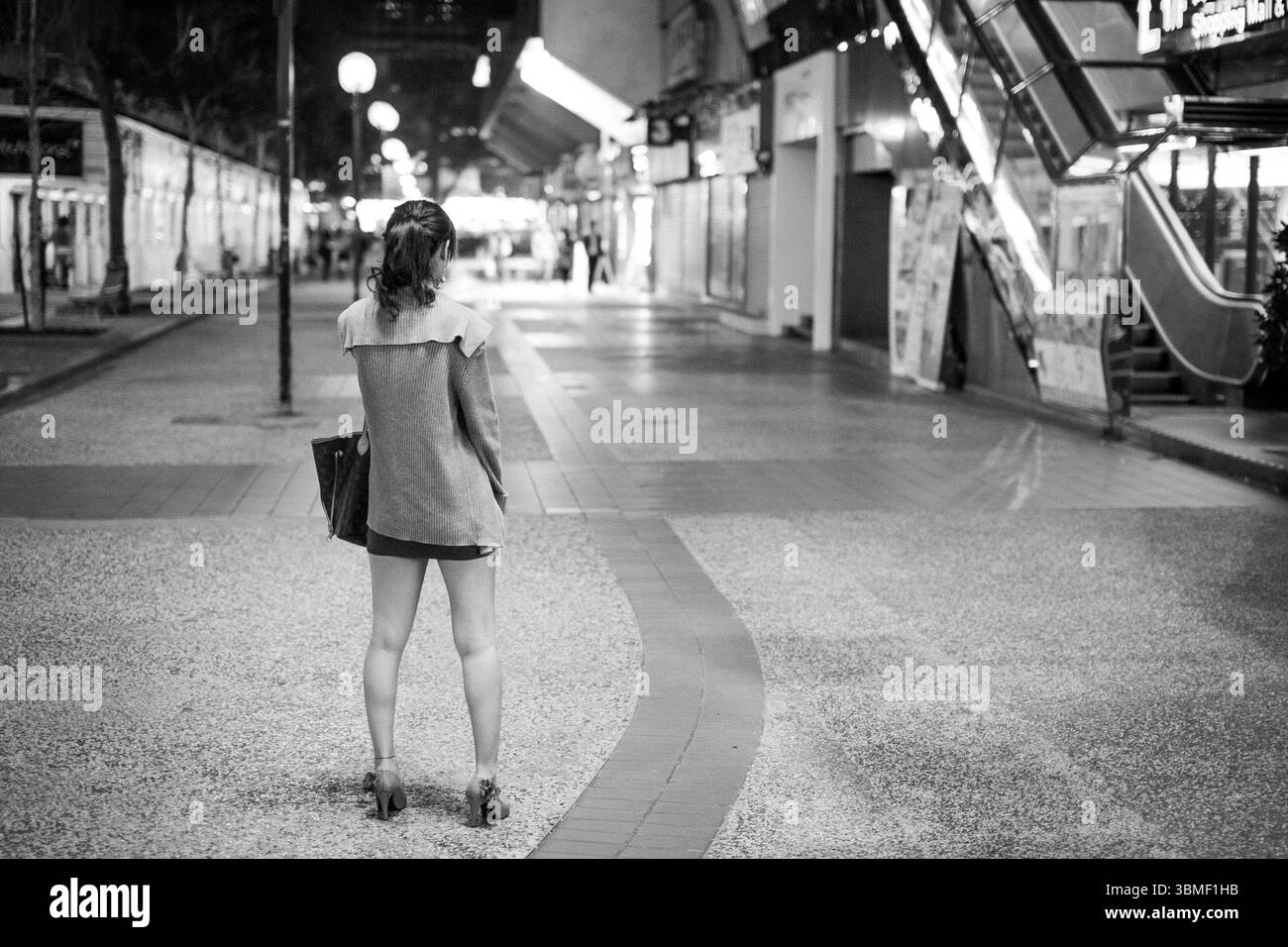Photo en noir et blanc capturant le dos d'une femme à Tsim Sha Tsui, Hong Kong, marchant à travers une zone urbaine calme, soulignant le contraste de Ligh Banque D'Images