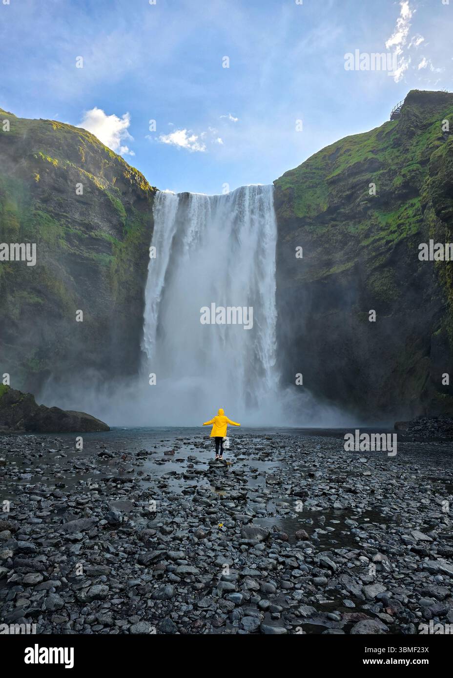 Admirez la puissante cascade de Skogafoss en Islande, où l'eau plonge de façon spectaculaire dans un paysage rocheux. femmes en imperméable jaune à une cascade Banque D'Images