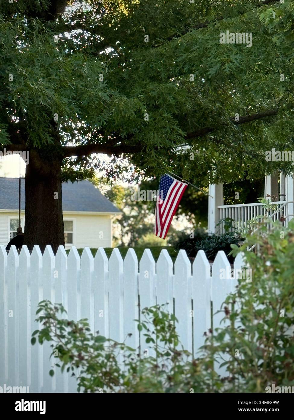 Un drapeau américain près d'une clôture blanche suspendue à un porche en été Banque D'Images