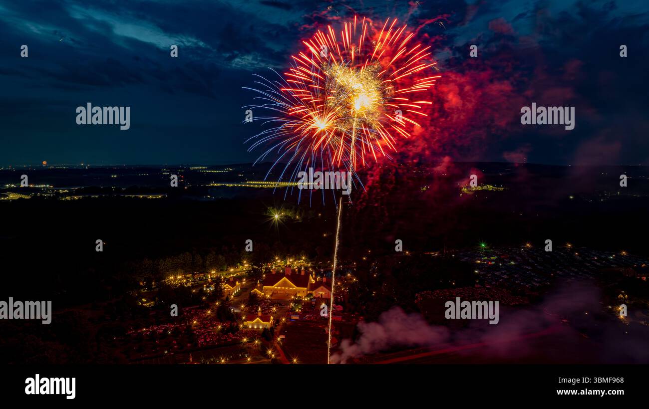Des feux d'artifice vibrants éclatent en différentes couleurs, éclairant le ciel nocturne lors d'un événement festif. Ci-dessous, un lieu magnifiquement décoré est entouré par exc Banque D'Images