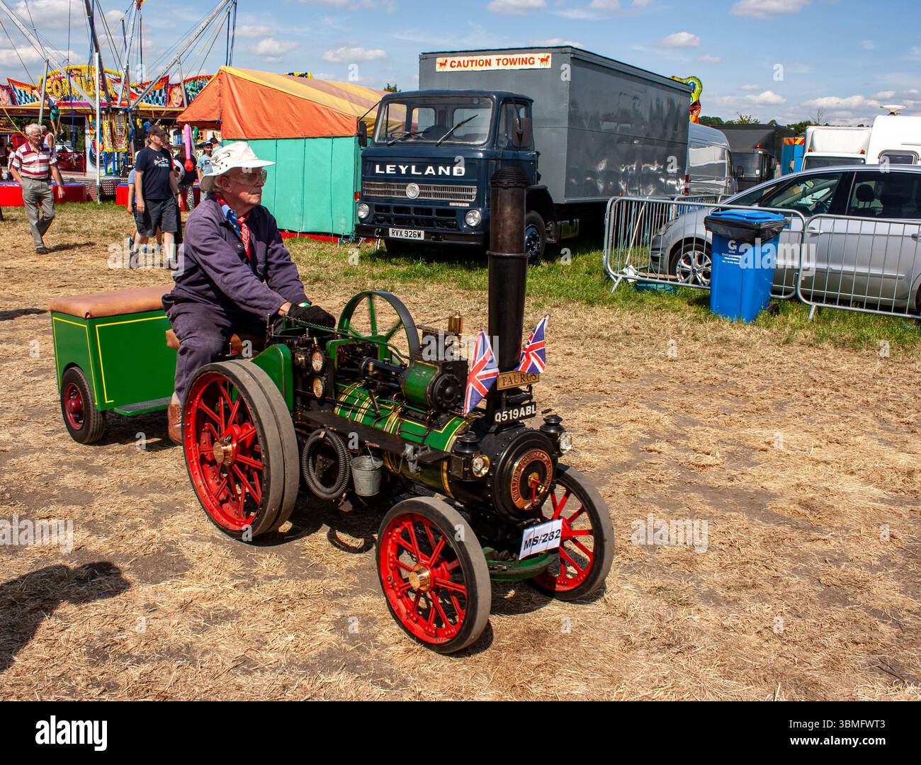 Un homme conduit un moteur de traction à vapeur miniature vintage orné de drapeaux britanniques dans un cadre de festival vintage en plein air Banque D'Images