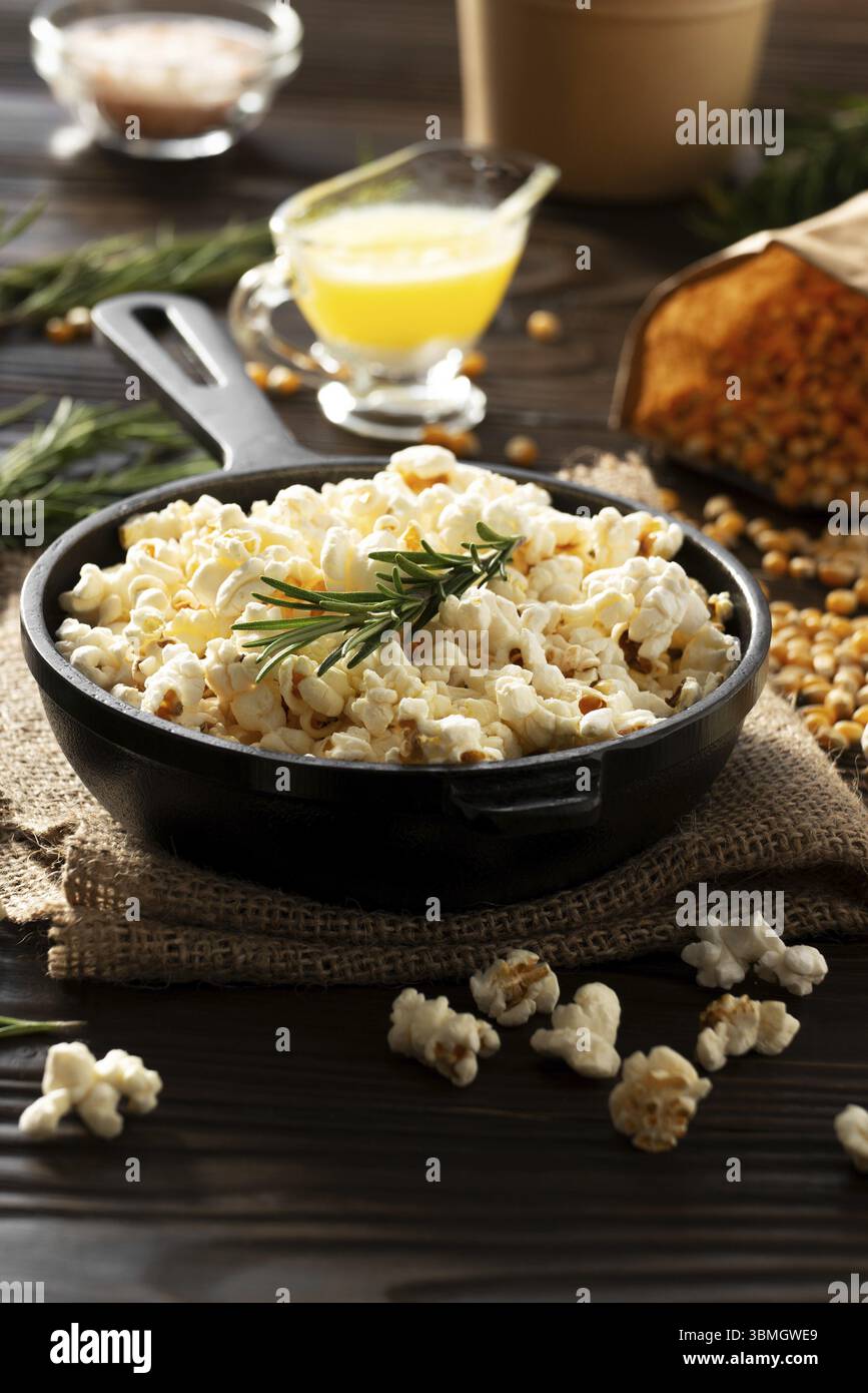 Pop-corn dans une poêle en fonte avec seau en papier et beurre fondu de côté Banque D'Images