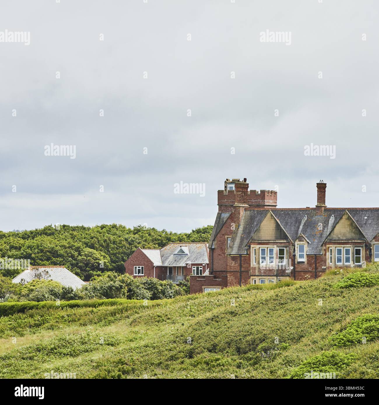 Une grande maison en briques sur une colline verdoyante avec beaucoup de végétation et un ciel nuageux. Bude, Cornouailles, Angleterre, Grande-Bretagne, Royaume-Uni, Europe Banque D'Images