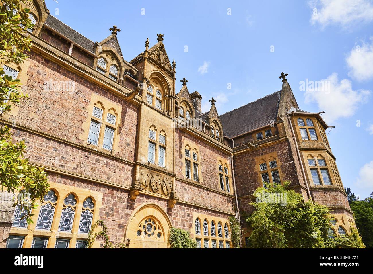 La façade impressionnante d'un bâtiment historique avec des éléments gothiques sur fond de feuillage vert et de ciel bleu. Knightshayes, Tiverton, Devon, en Banque D'Images