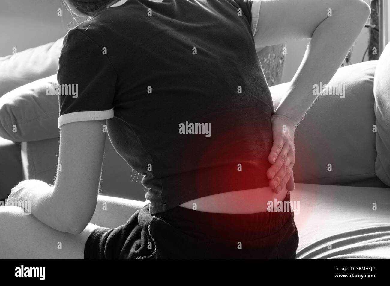 Fille tenant son bas du dos dans la douleur tout en étant assis sur le canapé - douleur de dos aiguë, mal de dos Banque D'Images