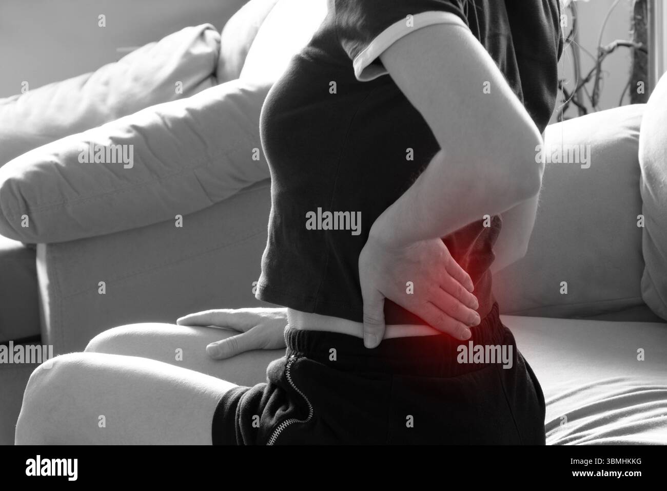 Fille tenant son bas du dos dans la douleur tout en étant assis sur le canapé - douleur de dos aiguë, mal de dos Banque D'Images