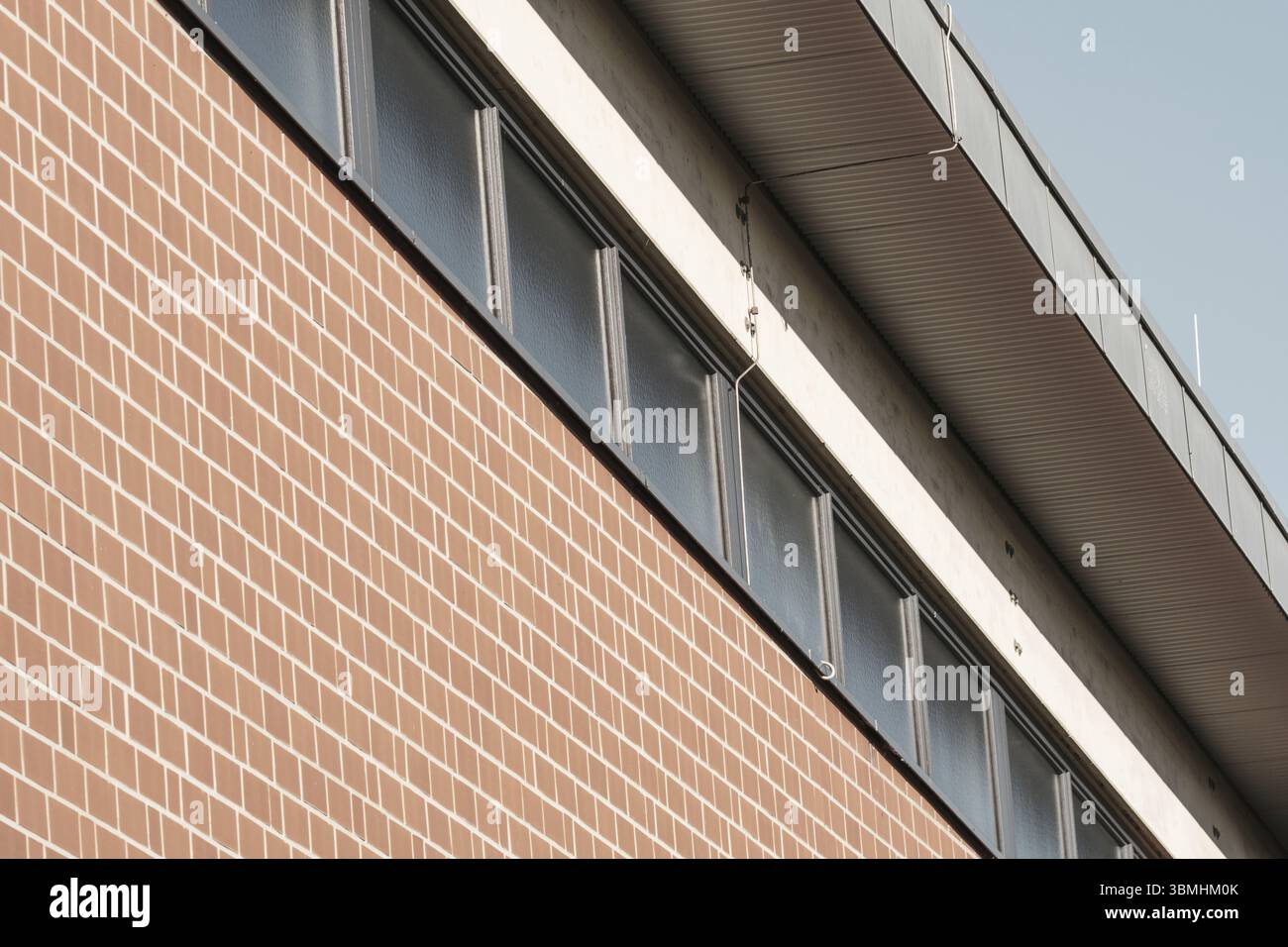 Mur de briques rouges s'élevant pour rencontrer le toit en métal et les fenêtres sur un bâtiment moderne, créant des lignes fortes et le contraste Banque D'Images
