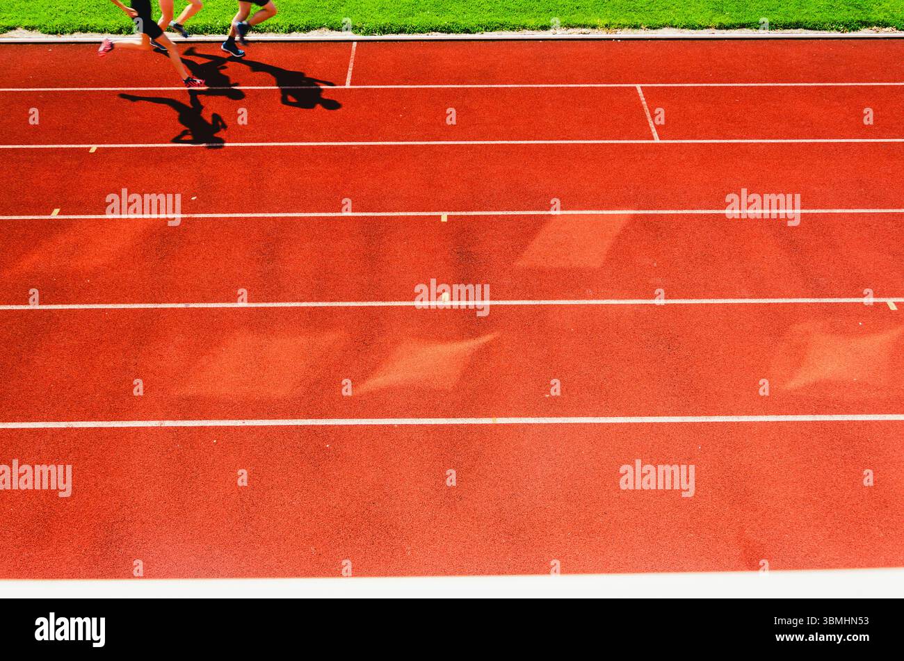 Illustration athlétique : les pieds d’un coureur et leurs ombres frappent la piste de tartan rouge en plein soleil Banque D'Images