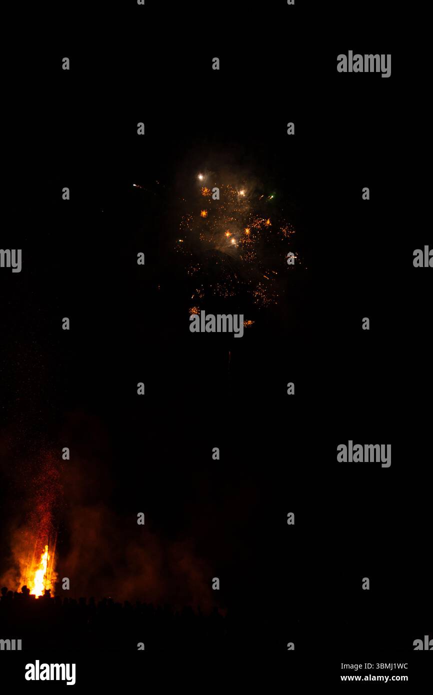 Des feux d'artifice aux couleurs vives éclatent dans le ciel étoilé tandis qu'un feu de joie crépite en dessous, créant une atmosphère captivante remplie d'excitation et de joie Banque D'Images