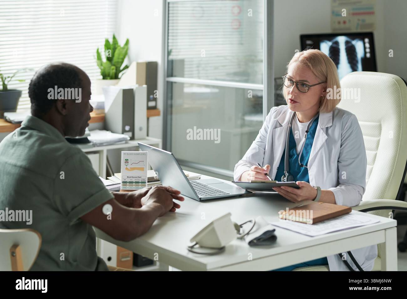 Homme noir d'âge moyen avec moniteur de glucose sur le bras consultant le médecin féminin caucasien d'âge moyen dans le cabinet médical, discutant de la gestion du diabète à Banque D'Images