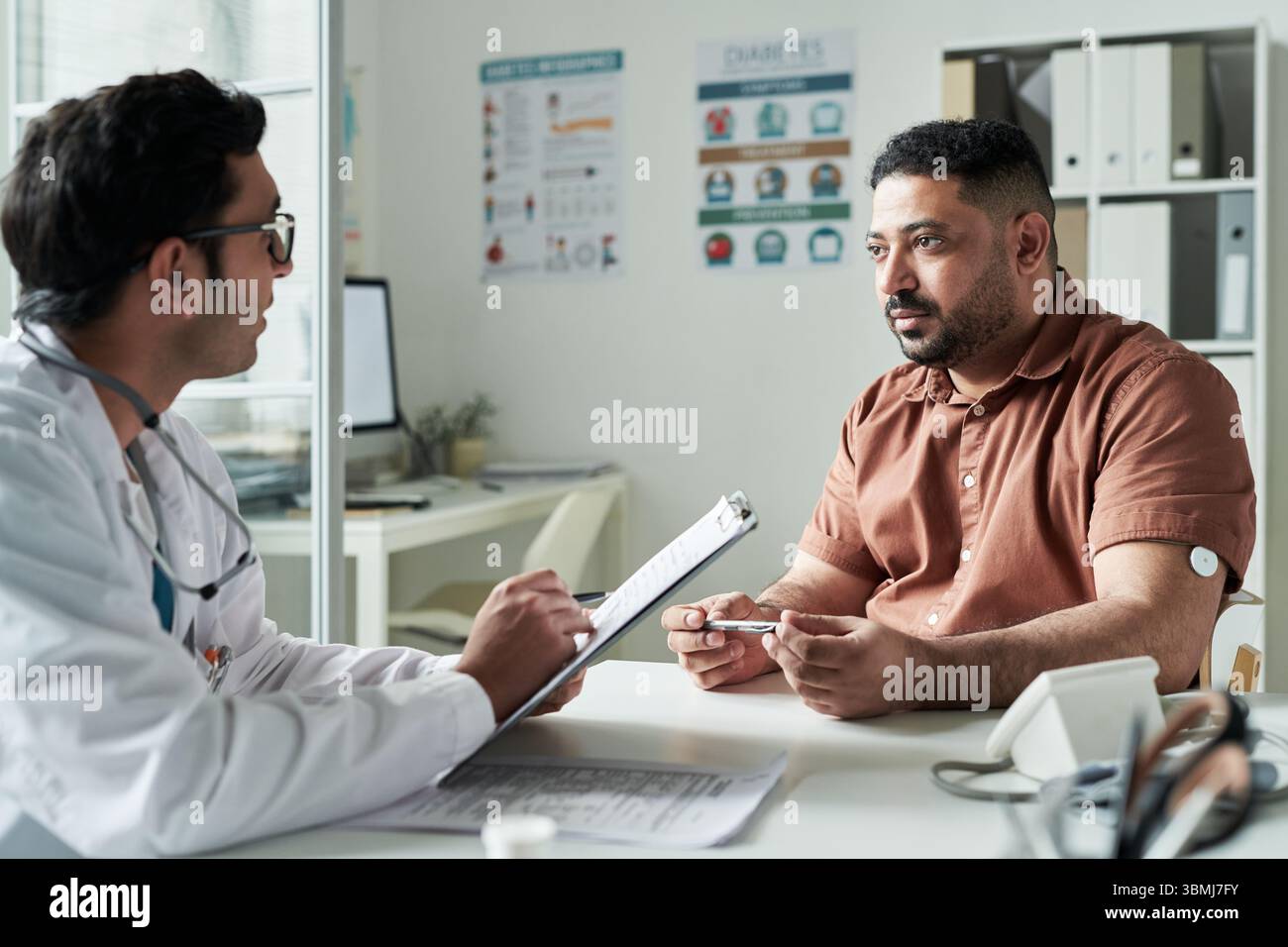 Homme caucasien d'âge moyen avec le diabète consultant médecin masculin dans le cabinet médical, patient tenant le glucomètre tout en discutant de la gestion de la santé, moi Banque D'Images