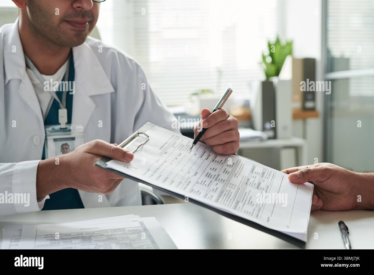 Docteur masculin caucasien d'âge moyen tenant la forme médicale tout en consultant un patient invisible dans le cabinet médical, médecin portant des lunettes et stéthoscope, pati Banque D'Images
