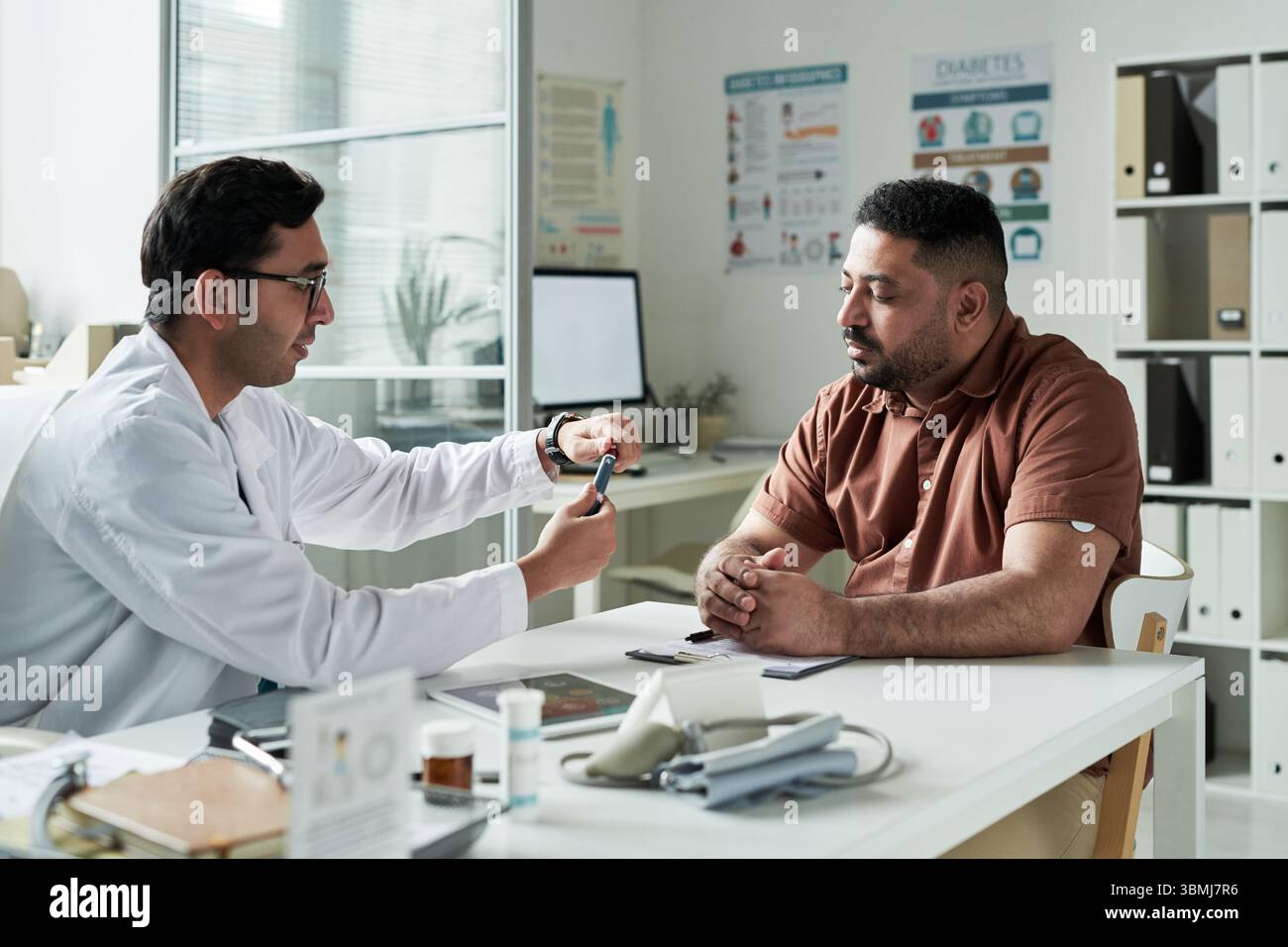 Médecin masculin caucasien d'âge moyen démontrant le glucomètre à l'homme noir d'âge moyen avec le diabète pendant la consultation médicale dans l'examen clinique moderne Banque D'Images