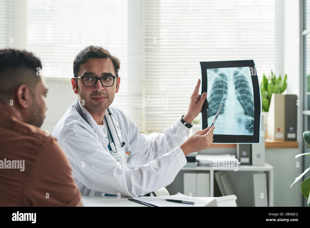 Médecin masculin caucasien d'âge moyen expliquant les résultats de radiographie thoracique à l'homme d'âge moyen pendant la consultation de diabète dans le cabinet médical, médecin tenant X-R. Banque D'Images