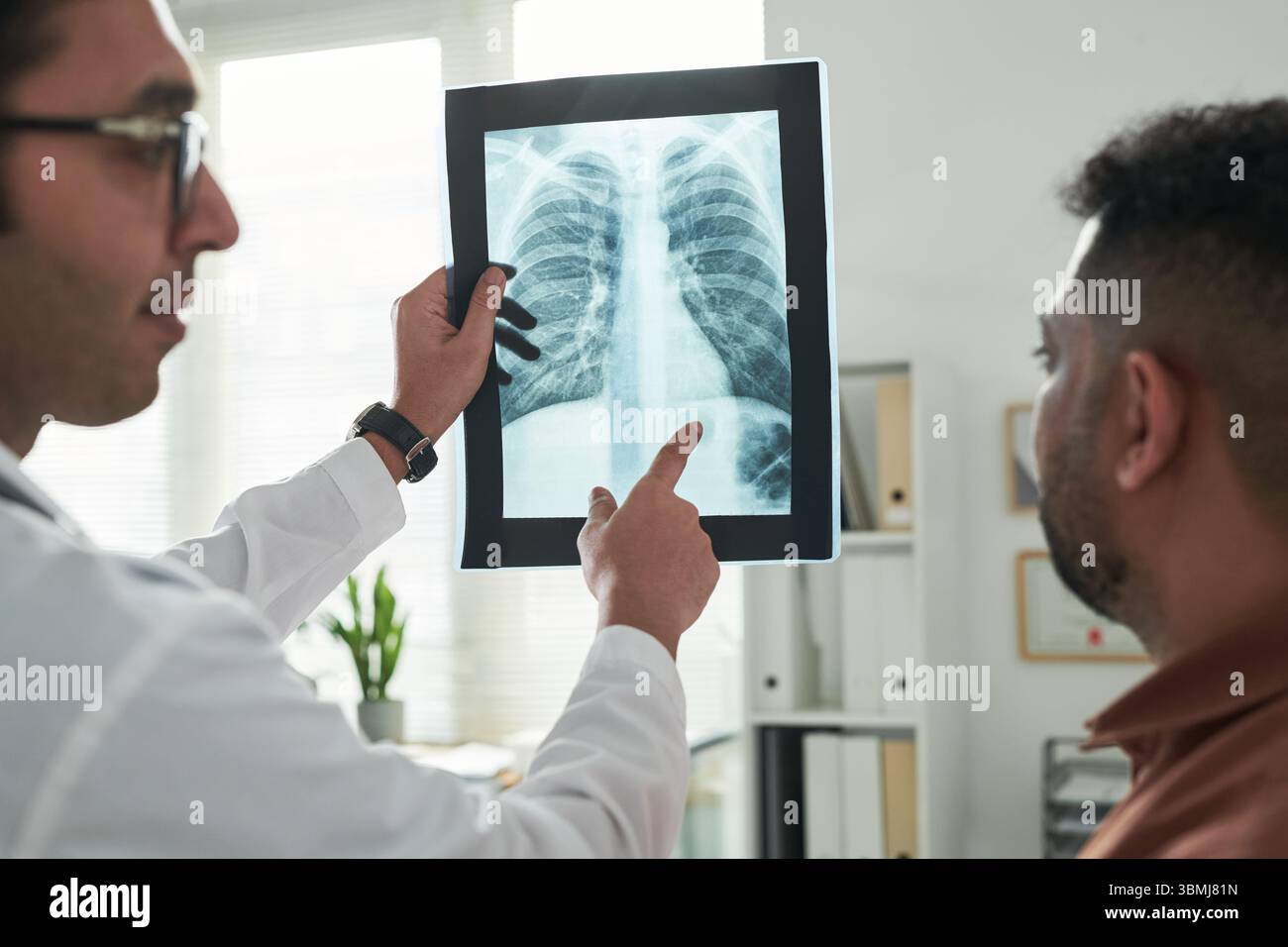 Docteur masculin caucasien d'âge moyen montrant et expliquant l'image de radiographie thoracique à l'homme noir d'âge moyen patient pendant la consultation de diabète dans le médical de Banque D'Images