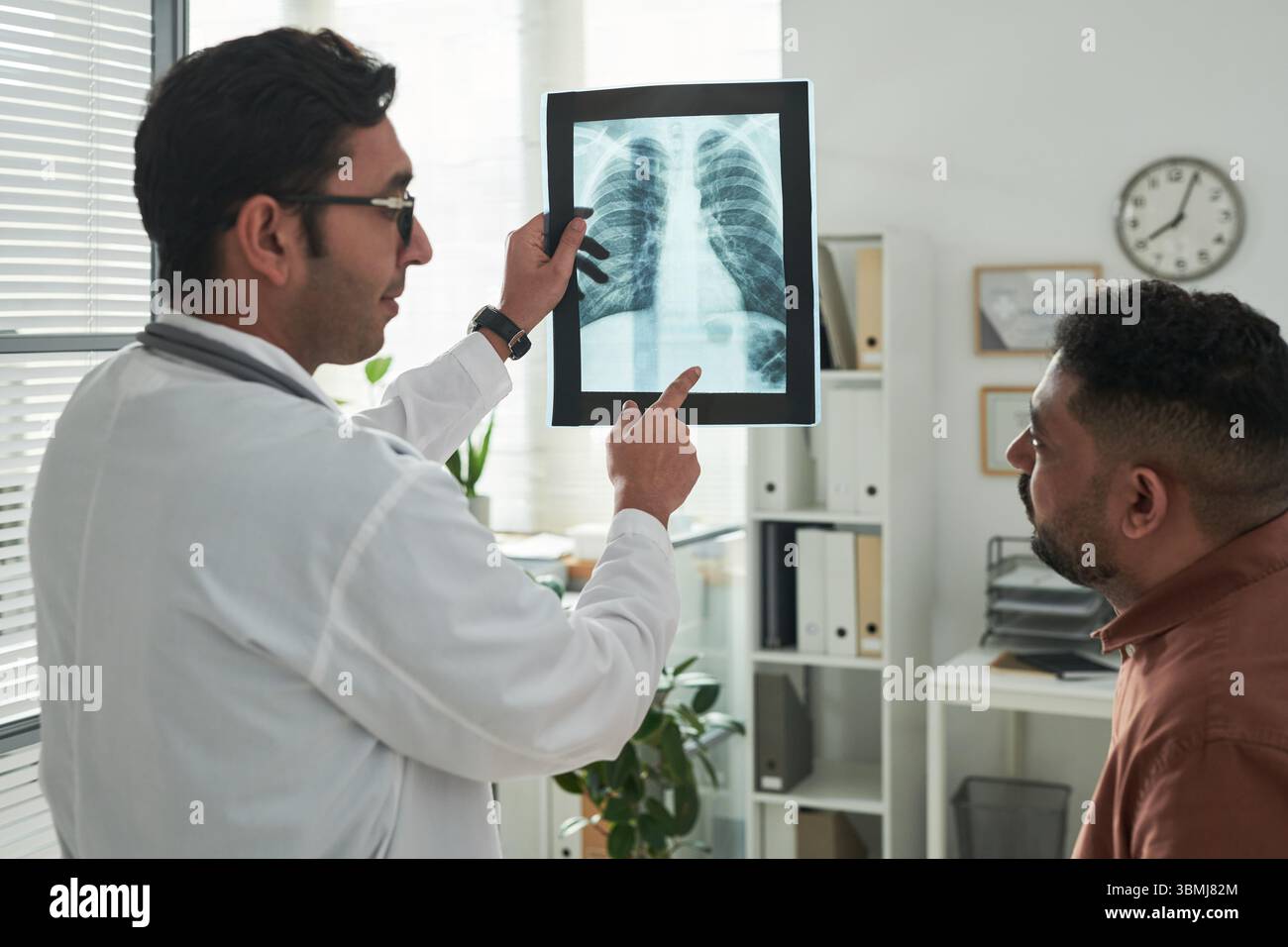 Médecin masculin caucasien d'âge moyen montrant la radiographie thoracique à l'homme noir d'âge moyen patient pendant la consultation médicale dans le cabinet, discutant du diabète rela Banque D'Images
