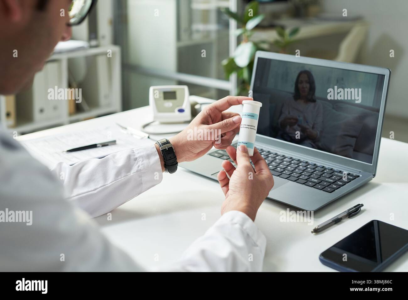 Docteur masculin caucasien d'âge moyen tenant la bouteille de médicament pendant la consultation de télémédecine avec le jeune adulte femme noire patient sur l'écran d'ordinateur portable, di Banque D'Images