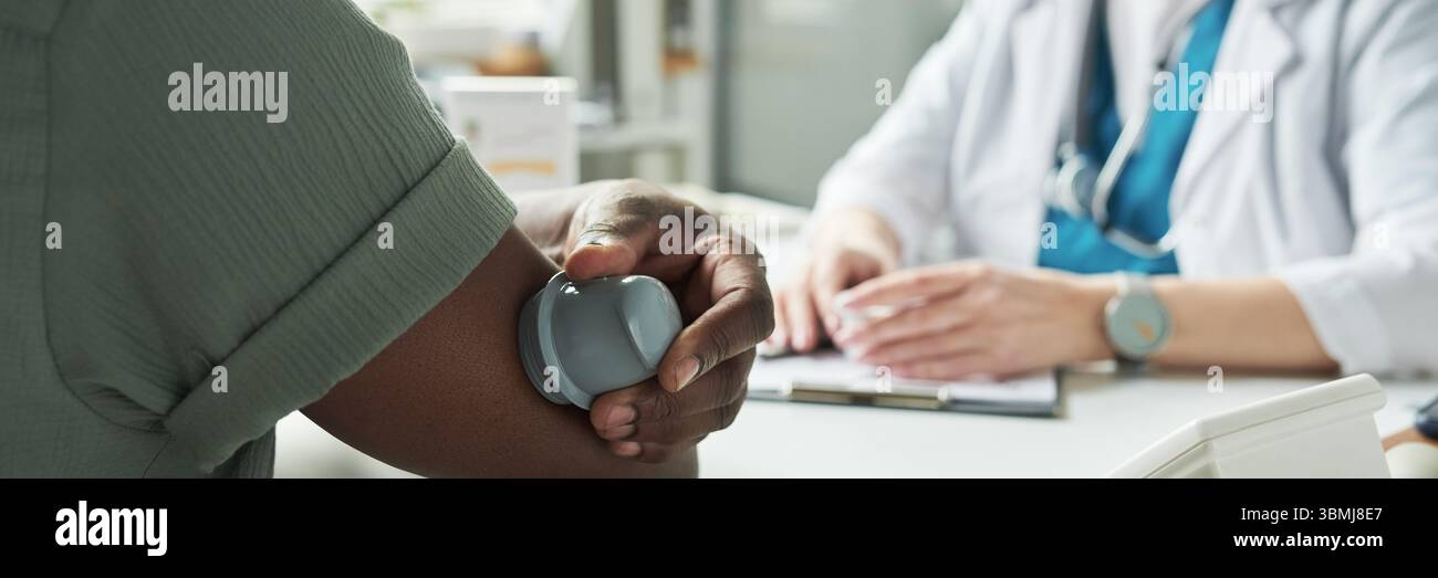 Homme noir d'âge moyen ayant la pression artérielle mesurée par un professionnel de la santé pendant la consultation de diabète dans le cabinet médical, médecin assis au bureau wi Banque D'Images