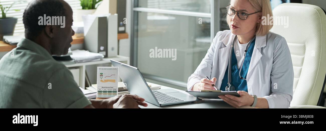 Homme noir d'âge moyen consultant le médecin féminin caucasien d'âge moyen dans le cabinet médical, discutant de la gestion du diabète Banque D'Images