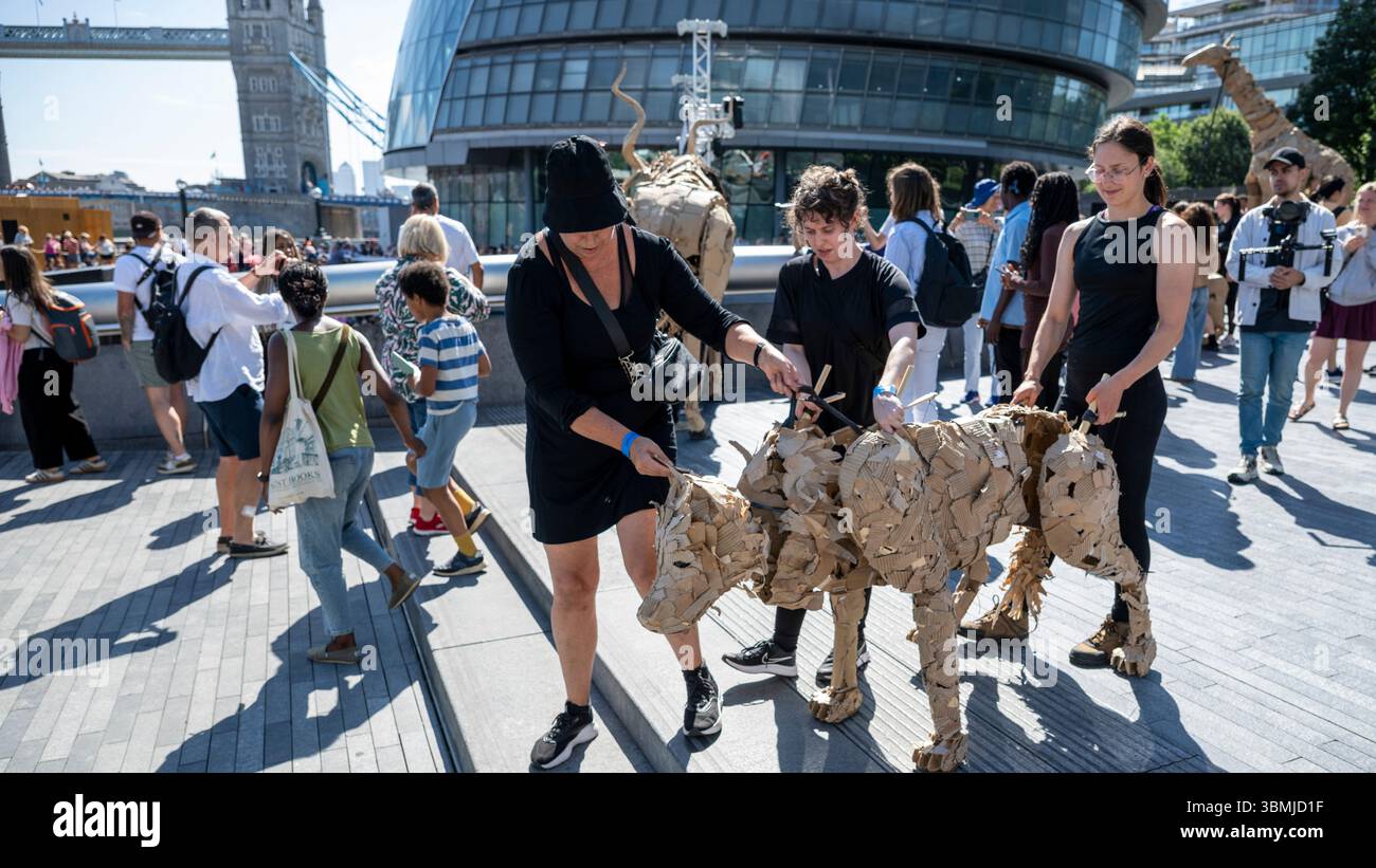 Londres, Royaume-Uni. 27 juin 2025. Les marionnettistes se produisent lors d’une conférence téléphonique près de Tower Bridge for THE HERDS, une nouvelle œuvre d’art majeure qui voit des animaux marionnettes grandeur nature voyager, d’avril à août 2025, sur une route de 20 000 km entre le bassin du Congo et le cercle arctique, symbolisant leur fuite d’une catastrophe climatique. Gorilles, lions, zèbres et kudus sont arrivés à Londres pour le week-end avant de passer à Manchester. Credit : Stephen Chung / Alamy Live News Banque D'Images