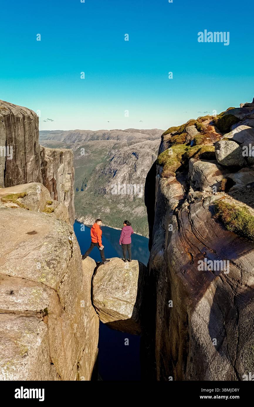 Deux aventuriers se tiennent sur une formation rocheuse au-dessus d'un fjord profond, entouré par la nature sauvage norvégienne à couper le souffle. Kjeragbolten Lysefjord, Norvège Banque D'Images