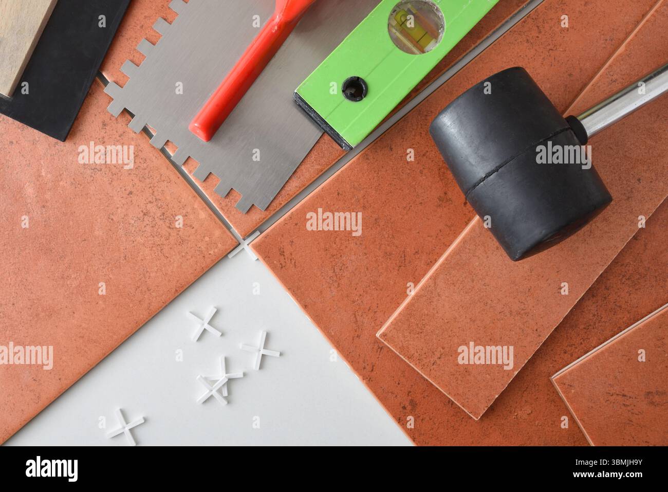 Tuiles placées avec des espaceurs sur une base blanche avec des outils sur le dessus tels qu'un pot, un niveau, une spatule et une truelle. Vue de dessus. Banque D'Images