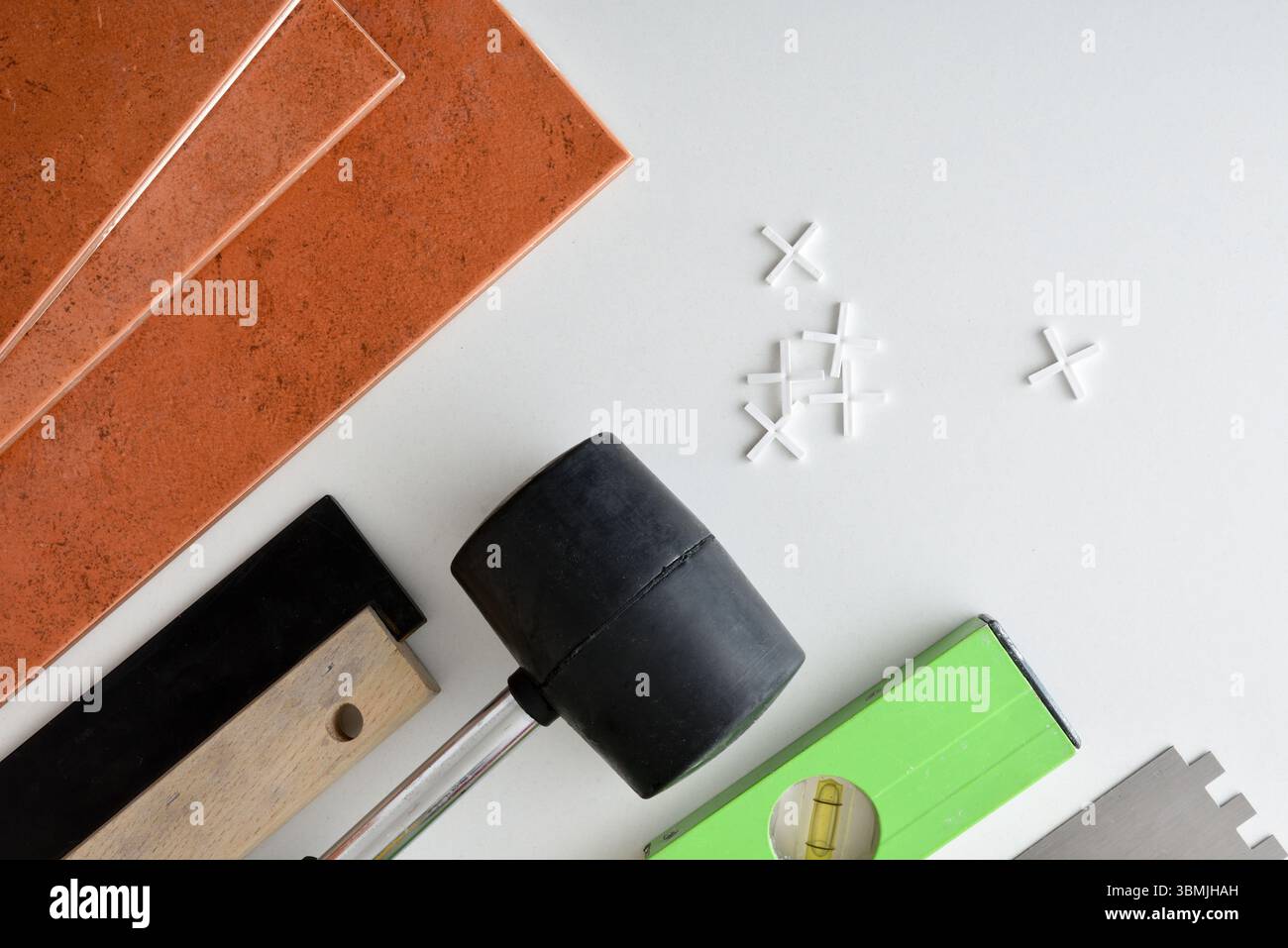 Tuiles brunes et outils pour les poser tels qu'un pot, une spatule de niveau et une truelle sur une table blanche avec des espaceurs. Vue de dessus. Banque D'Images