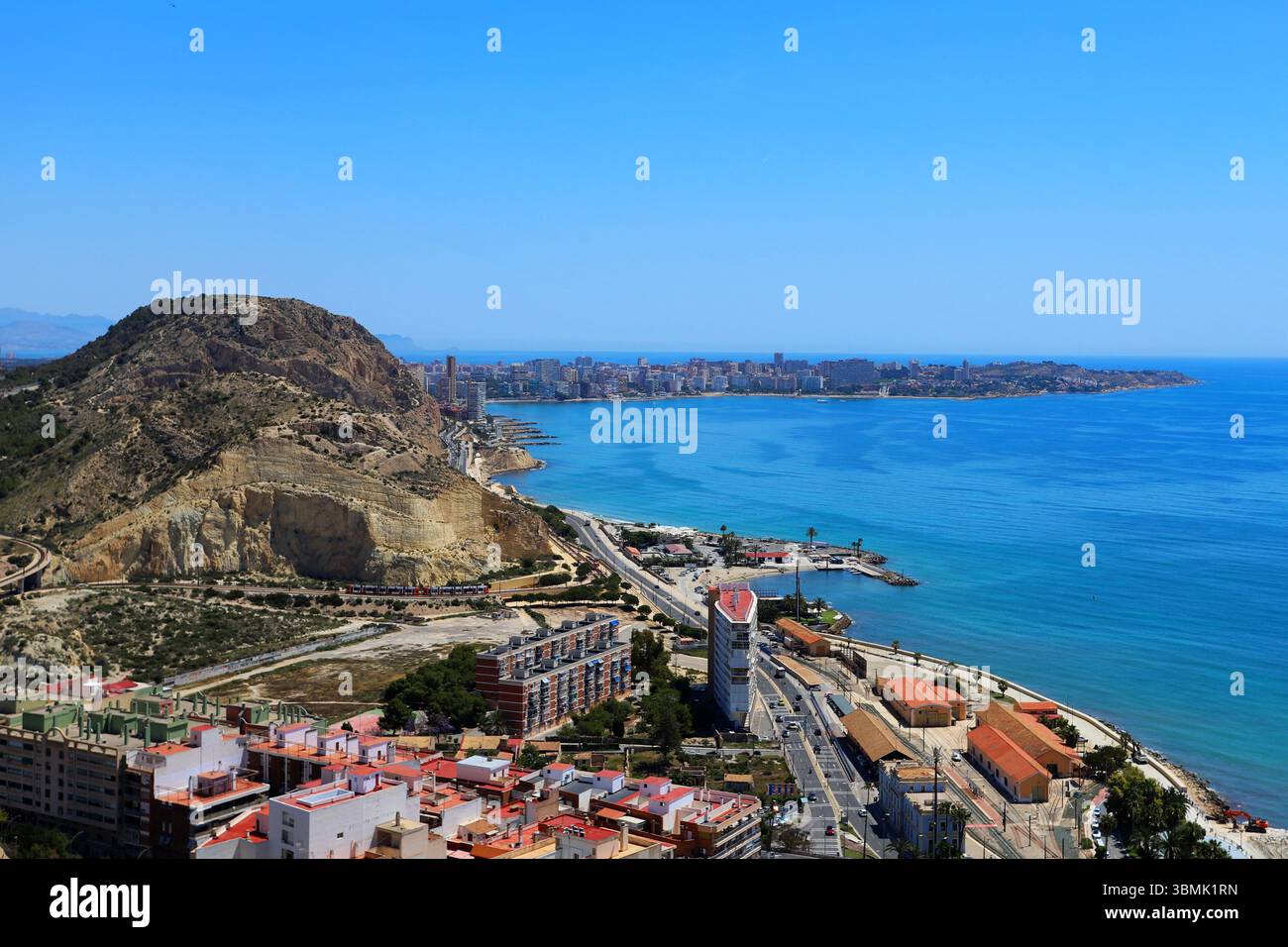 Vue sur la côte de la plage de Postiguet à Alicante avec mer bleue, hôtels modernes, palmiers et promenade en bord de mer. Banque D'Images