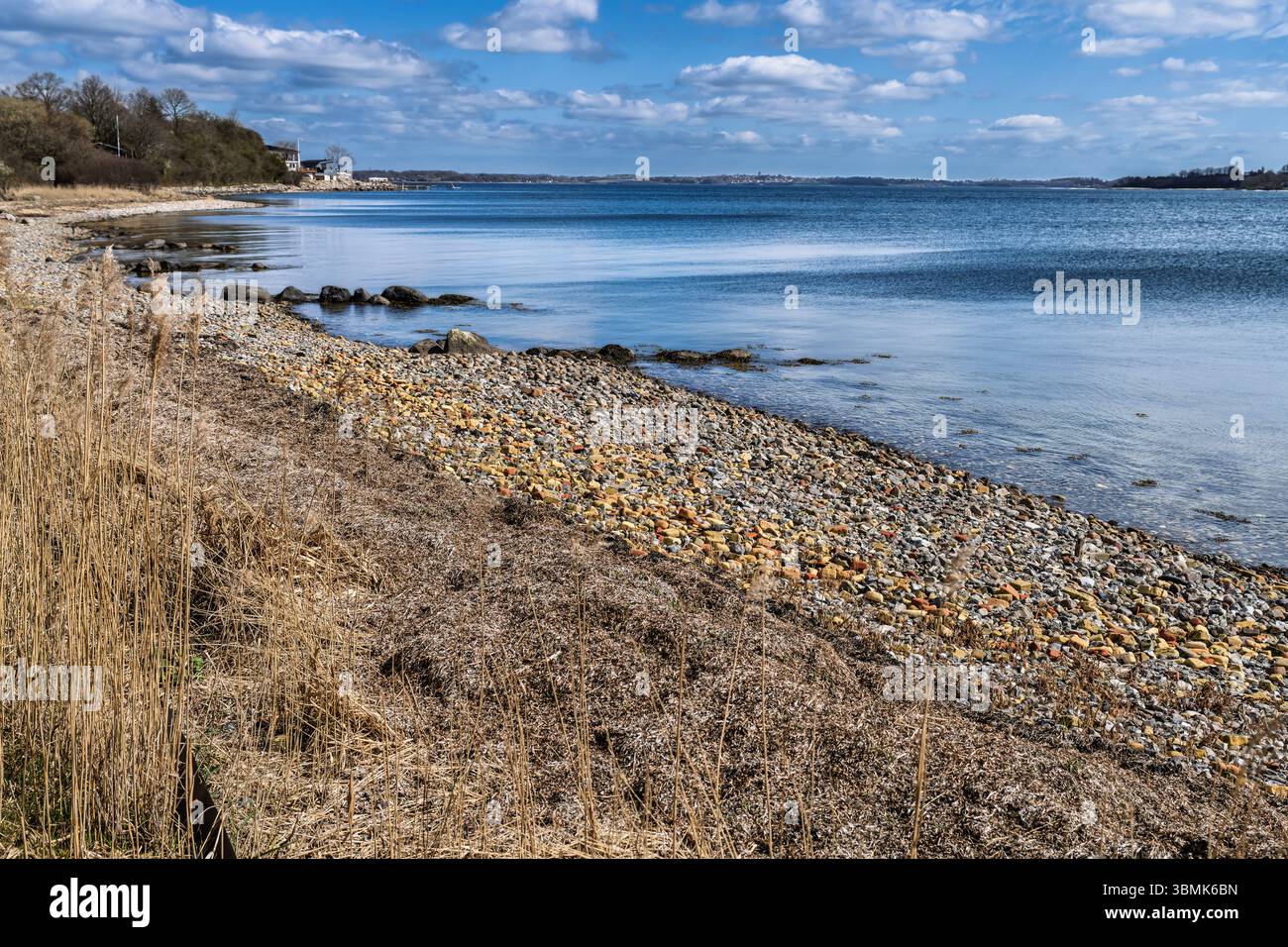 Vue calme sur le front de mer avec une étendue de rivage de galets bordée par des eaux de mer tranquilles sous un ciel bleu clair avec de légers nuages, créant un Ser Banque D'Images