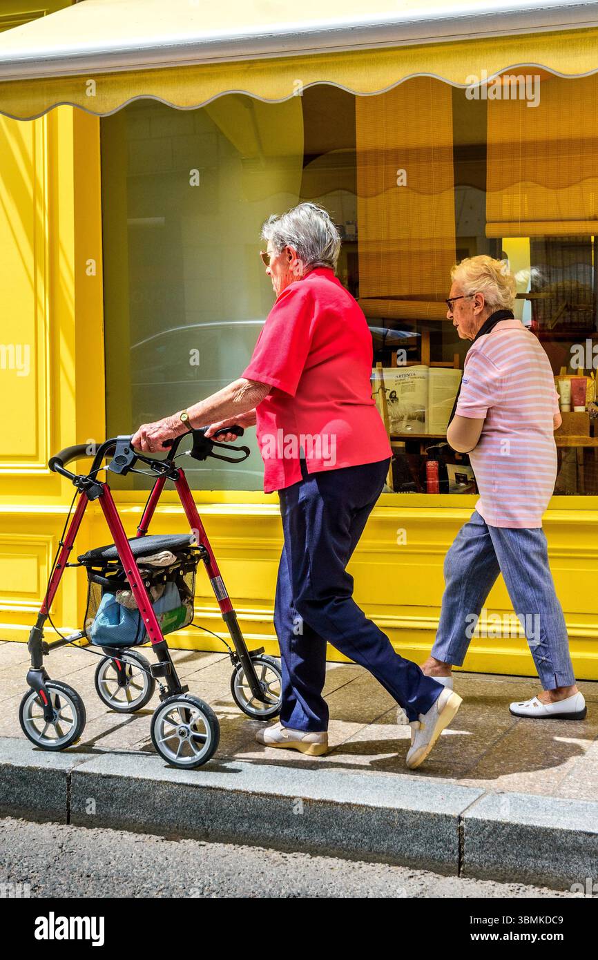 Deux femmes plus âgées - une avec aide à la marche à roulettes - marchant le long du trottoir - Loches, Indre-et-Loire (37), France. Banque D'Images