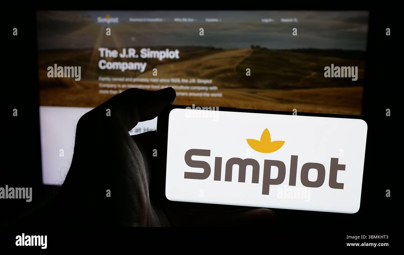 Stuttgart, Allemagne - 04-26-2025, personne tenant un téléphone portable avec le logo de la société agro-alimentaire américaine J. R. Simplot sur l'écran en face de la page web. Banque D'Images