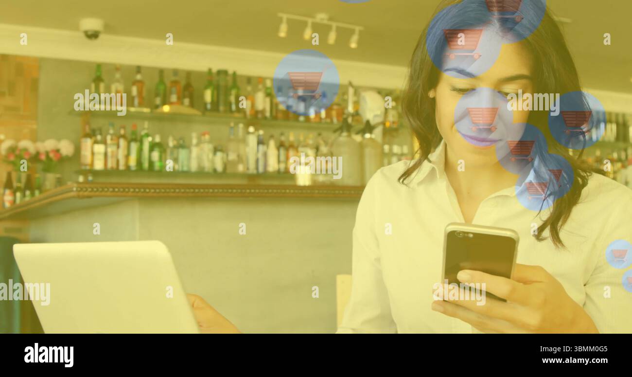 En utilisant smartphone et ordinateur portable, femme voyant l'image du panier dans le café Banque D'Images