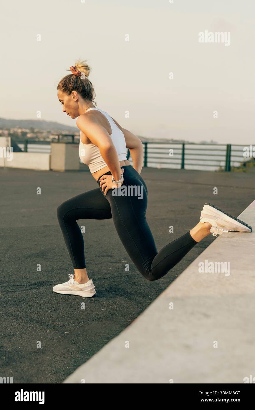 Une femme athlétique effectue un squat fractionné bulgare, un type de fente sur une jambe, pendant son entraînement de musculation en plein air. Banque D'Images