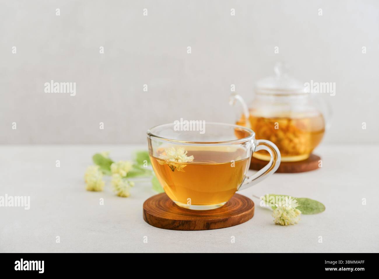 Tasse en verre de thé tilleul avec théière en verre et fleurs tilleul sur fond clair Banque D'Images