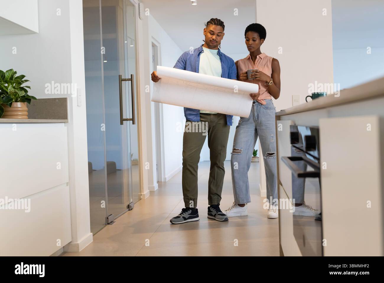 Examen couple debout dans le couloir de la maison moderne, avec plan roulé et smartphone Banque D'Images