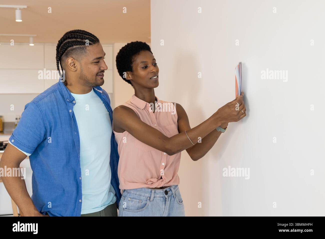 Couple diversifié plaçant le cadre d'image coloré sur le mur blanc dans le salon de la cuisine à domicile, avec décor Banque D'Images