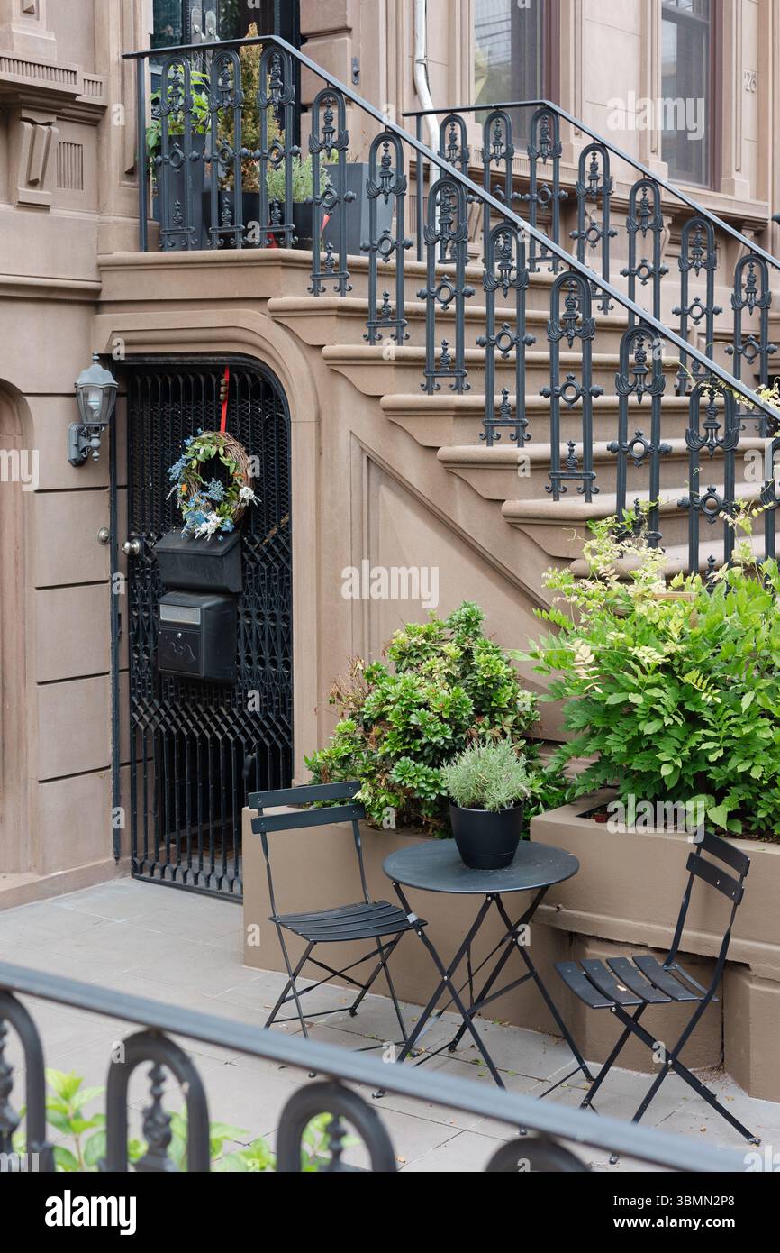 Disposition confortable des sièges avec des plantes et une couronne près d'une entrée élégante en grès brun dans une rue calme. Banque D'Images