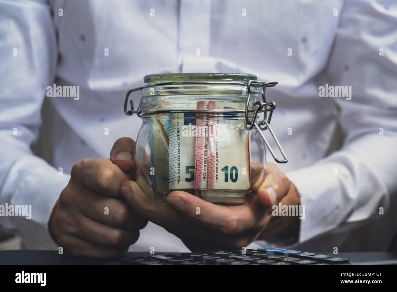 Les mains de l'homme comptant les billets de banque de dépenses de l'euro en espèces du pot en verre dans la tirelire sur la calculatrice. Gros plan des mains méconnaissables homme d'affaires. Enregistrer Banque D'Images