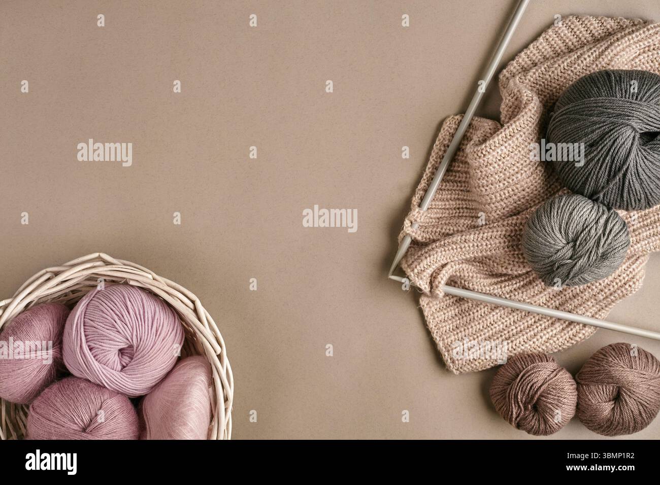 Boules de fil de laine mérinos, tricot sur aiguilles à tricoter sur une surface de couleur beige. Rose, blanc et gris de la balle de thread dans le panier. Vue d'en haut. La vie encore. C Banque D'Images