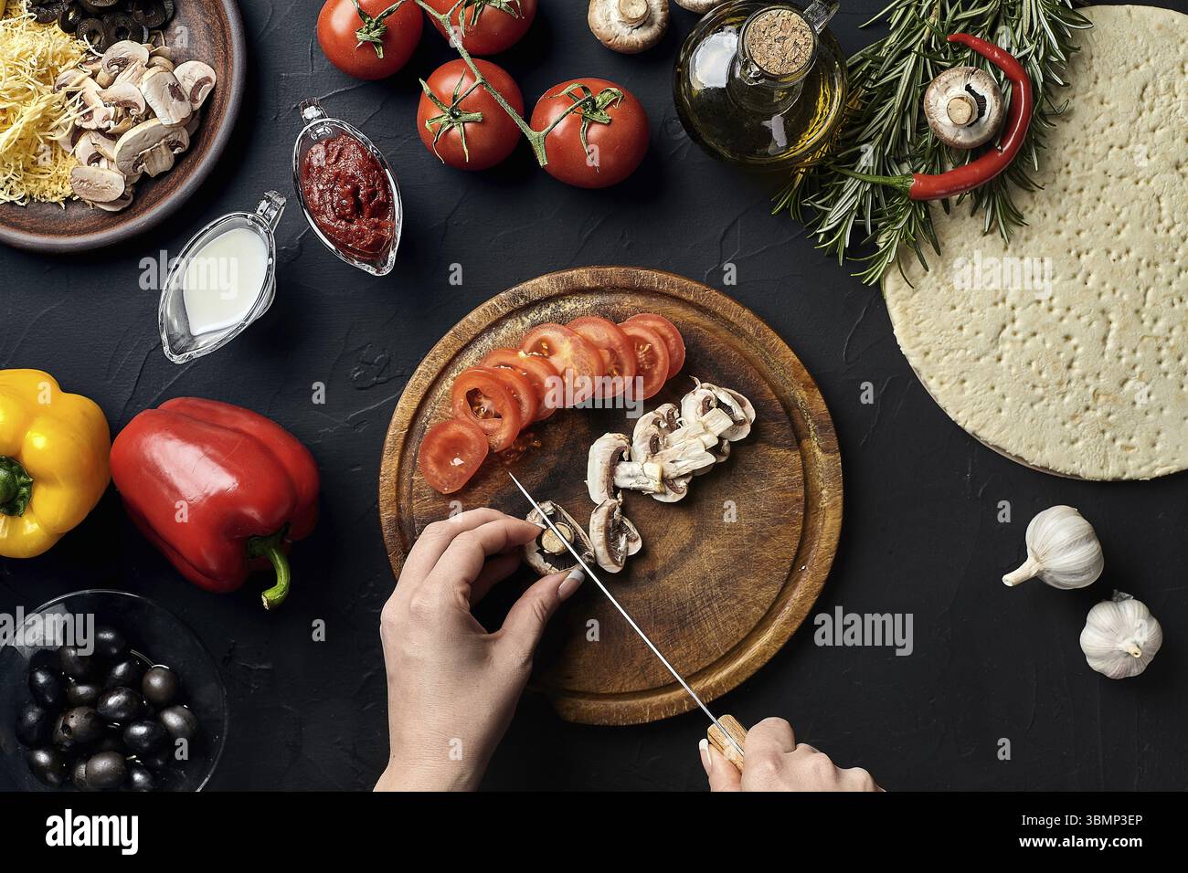 Femme coupe de main les champignons et les tomates sur planche de bois sur la table de cuisine, autour de mensonge ingrédients pour pizza : des légumes, du fromage et des épices. L'alimentation saine Banque D'Images
