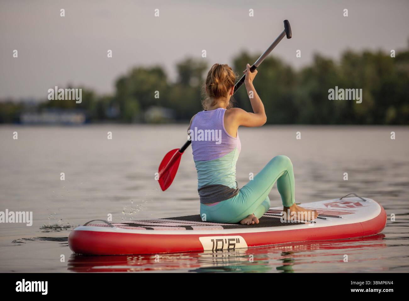 Sporty woman in yoga position sur le paddleboard, faisant du yoga sur le conseil sup, l'exercice de flexibilité et étirement des muscles. Woman practicing yoga on th Banque D'Images
