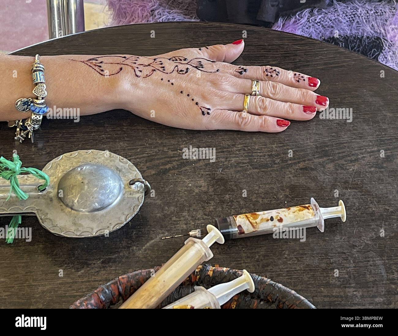Femme montrant un tatouage de henné frais sur la main avec des seringues et un récipient de henné sur une table en bois Banque D'Images