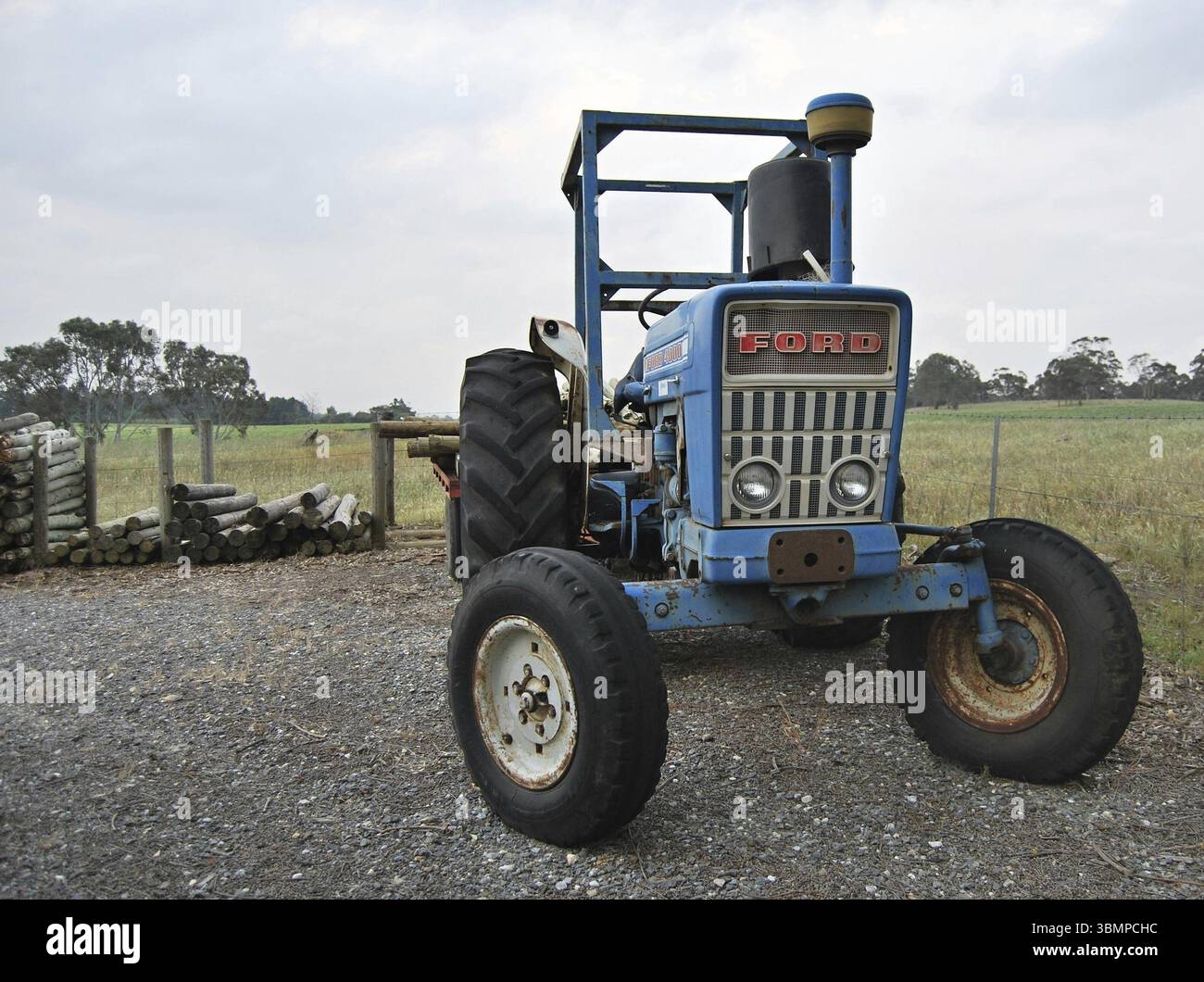 Vieux tracteur Ford bleu transportant des poteaux en bois garés dans un paysage rural Banque D'Images